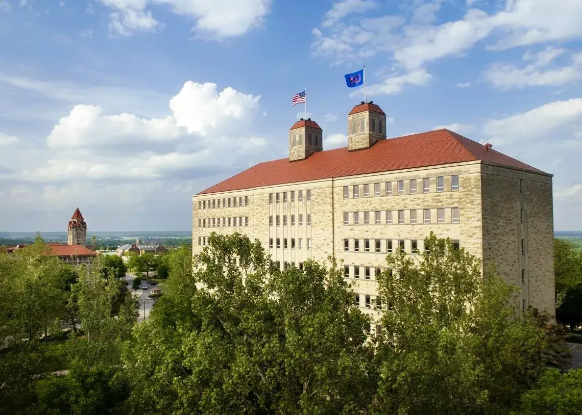 Fraser Hall on the University of Kansas campus in Lawrence, KS, with flags flying above its red roof