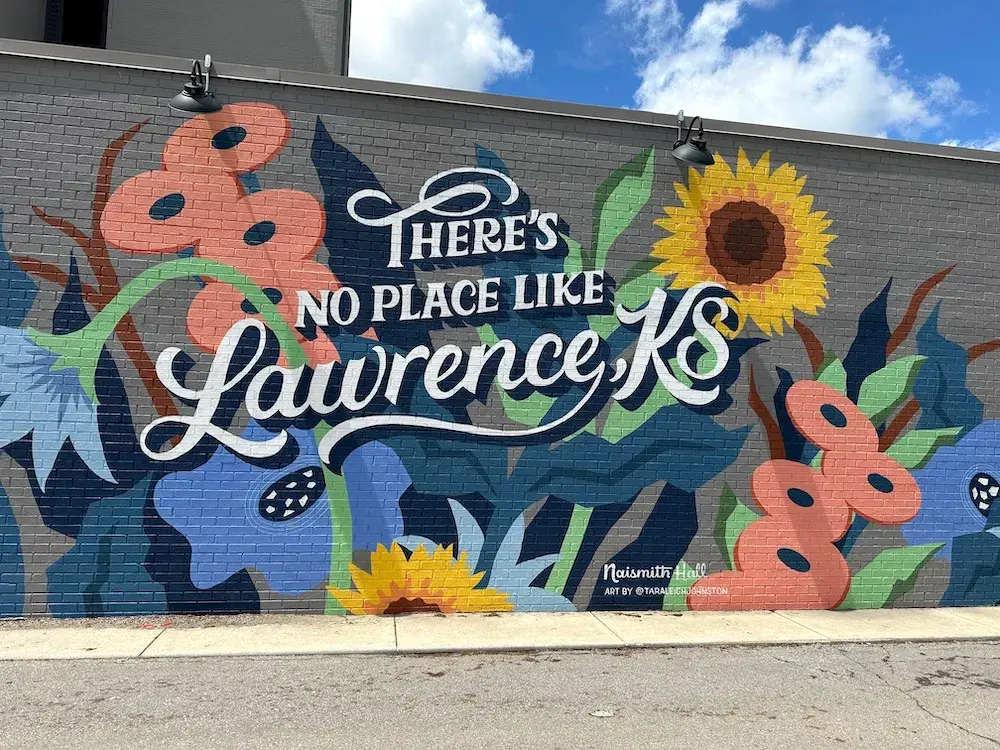 Mural reading There's No Place Like Lawrence, KS with painted sunflowers